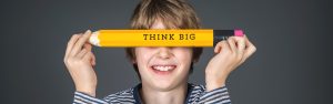 Ein Junge hält einen sehr großen Stift mit der Aufschrift "Think Big" vor seinem Gesicht