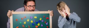 Die Schulbegleitung hält verzweifelt eine Tafel während ein Junge genervt guckt